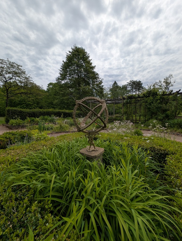 A statue in the middle of the garden of a man with the heavens on his back. 