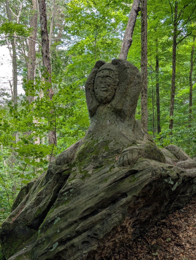 The form of a sphinx carved out of sandstone. She is weathered by the wind and her face is hard to see but her paws are clear.