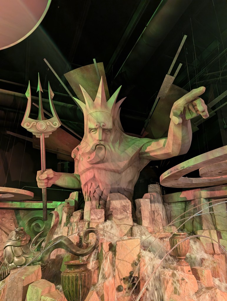 A very large sort of art deco statue of King Neptune holding a trident and pointing to the side. There are several streams of water flowing in front of him.