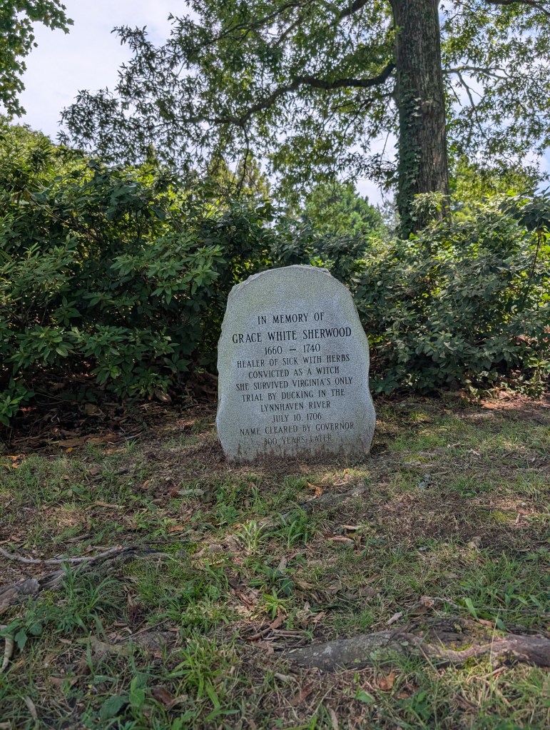 A rounded stone monument nestled against a green hedge. It is in memory of Grace White Sherwood.