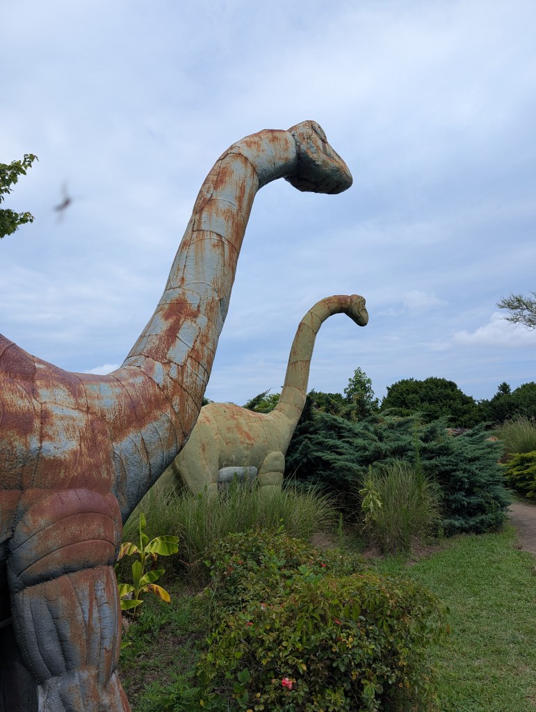 Two metal long-neck dinosaur statues stand almost side by side and look into the far distance. They look big and graceful.