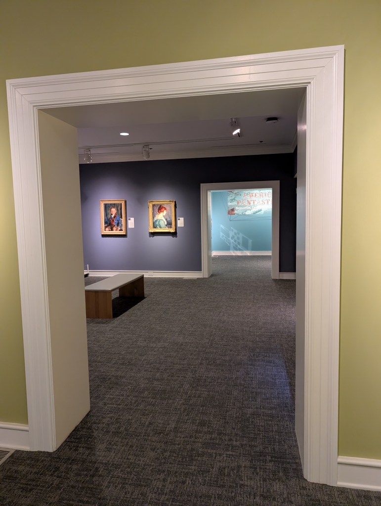 A view through two doorways in an art museum that shows two paintings in the middle room