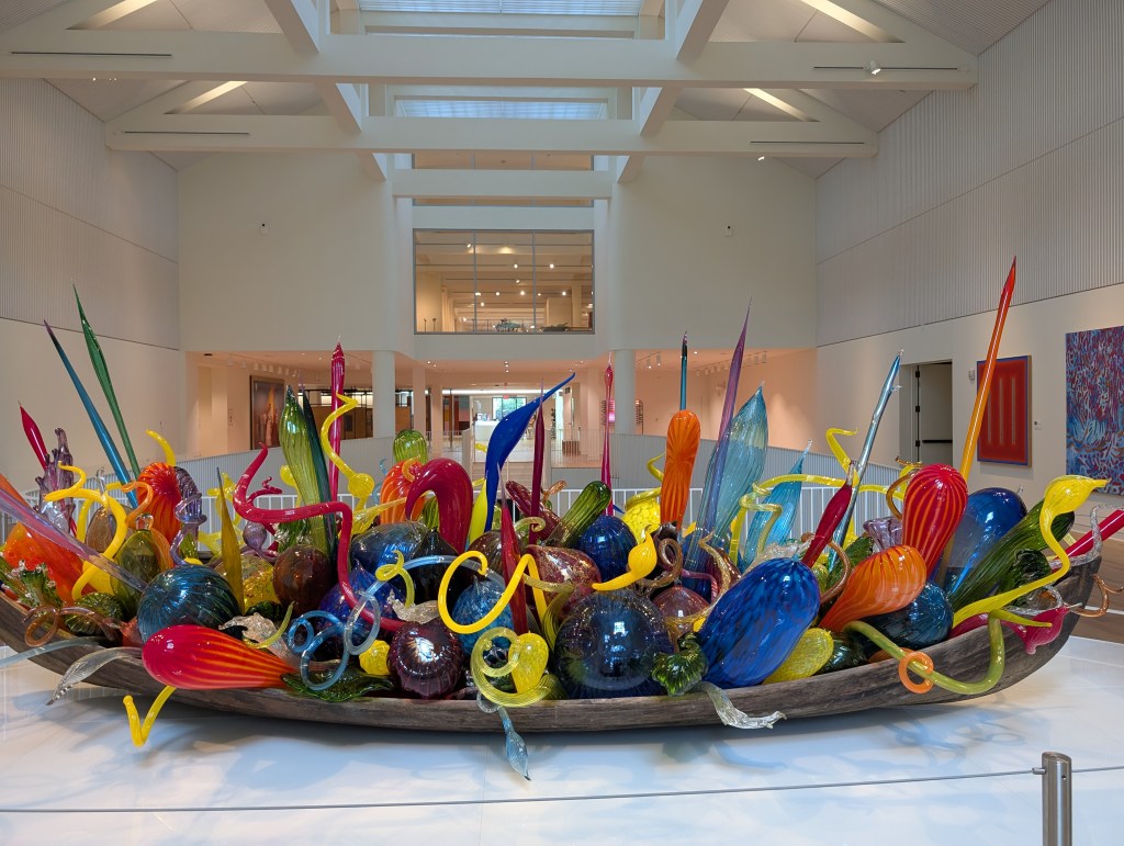 A very large wooden boat that is filled with colorful blown glass that looks like party balloons. The glass is twisted and shaped.