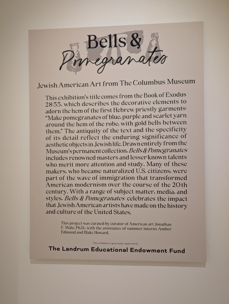 A sign explaining that the title "Bells & Pomegranates" comes from Exodus 28:33 and explains more about the exhibit