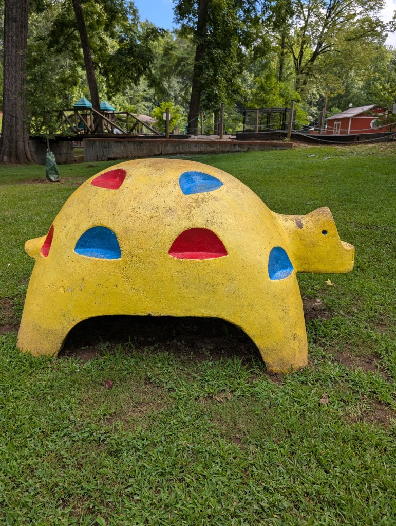 A yellow concrete figure that might be a turtle. It has red and blue cut-outs a climbing kid could use as footholds.