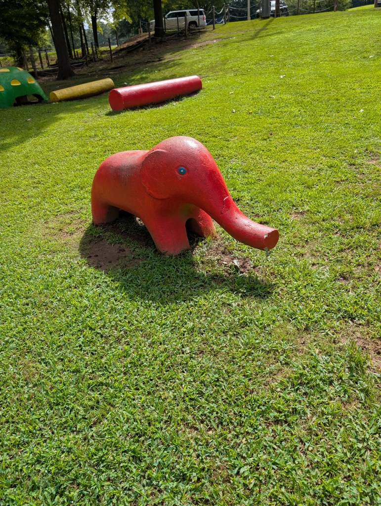 A tiny little bright red concrete baby elephant with a little blue eye. It is adorable.