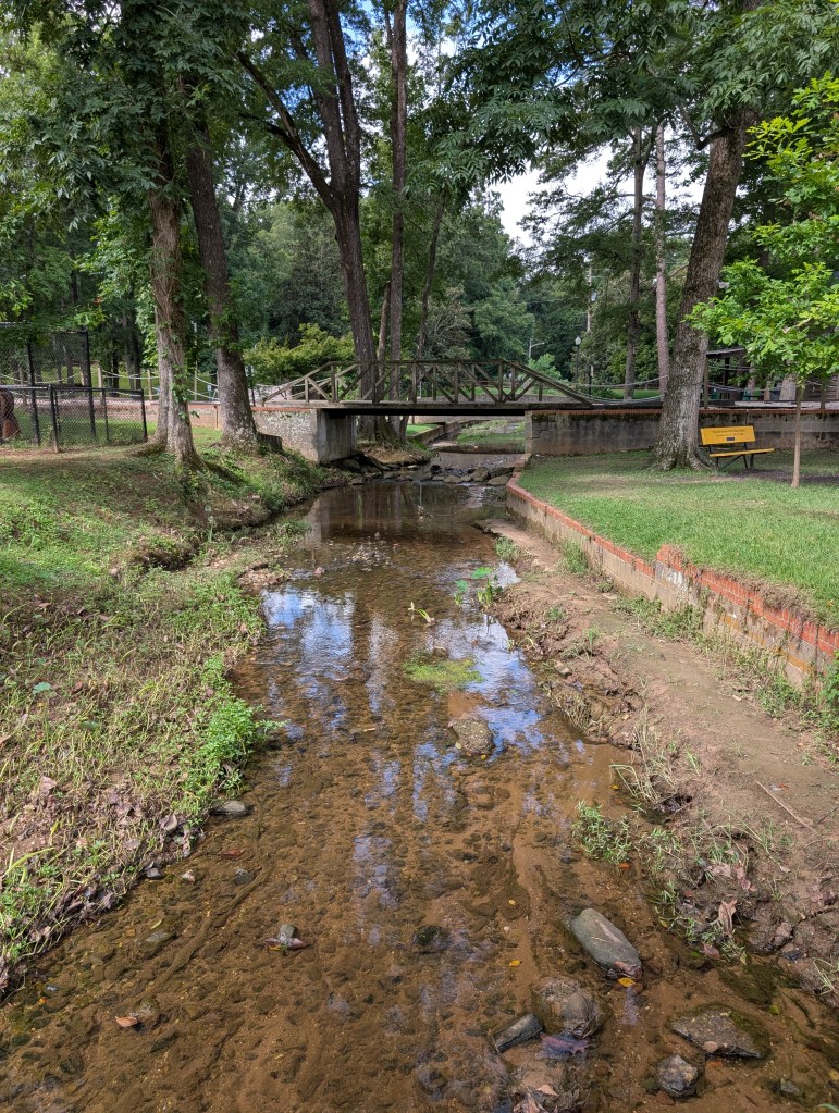 A shallow, rocky creek runs under a railroad bridge made for a small train.