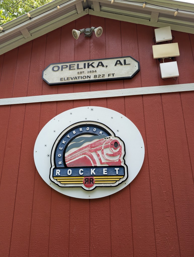 The side of a red slat barn that has a logo of a red train with "Rocky Brook Rocket" on it. Above it reads "Opelika, AL, Est. 1854, Elevation 822 FT".