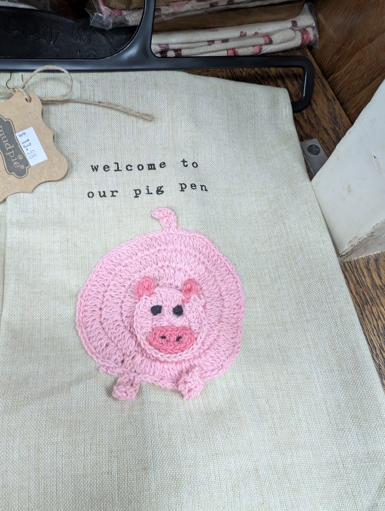 A decorative hand towel with a crochet (maybe?) pink pig on the front and the words "welcome to our pig pen" printed on it.