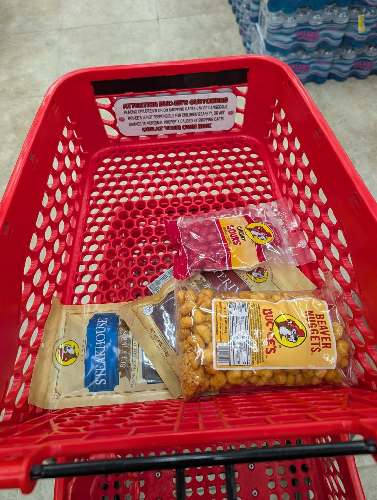 A red shopping cart with cherry sours, two bags of jerky, and a bag of Beaver Nuggets in it.