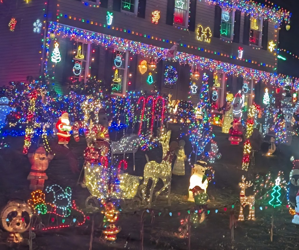 A house almost completely covered with Christmas lights. There are many inflatables and light-covered standups in the yard, as well. It's kind of a riot of yellow and red and green lights.